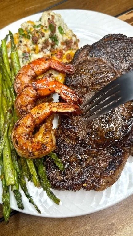 Steak dinner with loaded mashed potatoes, shrimp, and asparagus on a plate